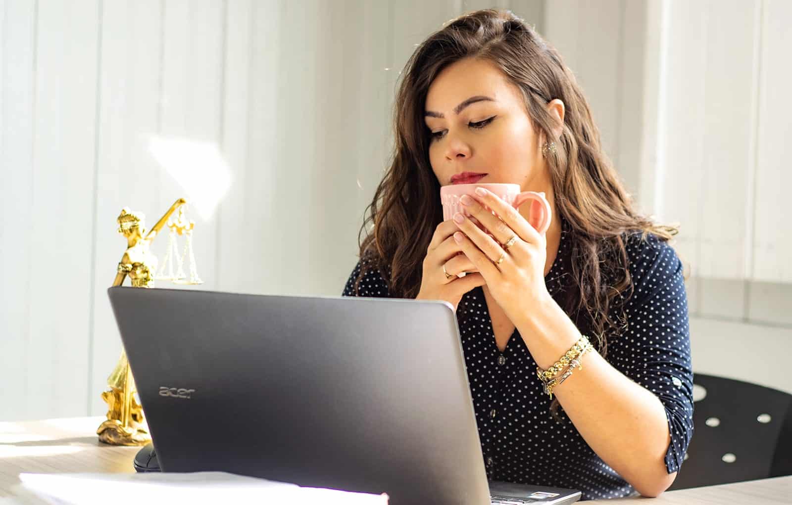 Woman drinking coffee looking at computer screen